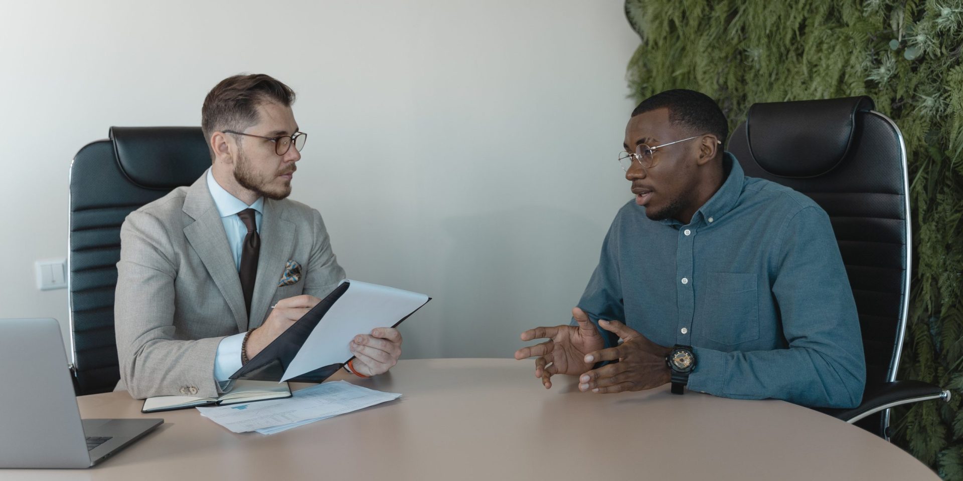 Two men engaged in a behavioral interview, seated at a table, discussing professional experiences and skills.