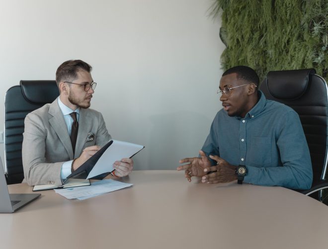 Two men engaged in a behavioral interview, seated at a table, discussing professional experiences and skills.