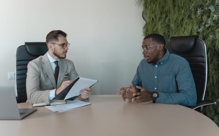 Two men engaged in a behavioral interview, seated at a table, discussing professional experiences and skills.
