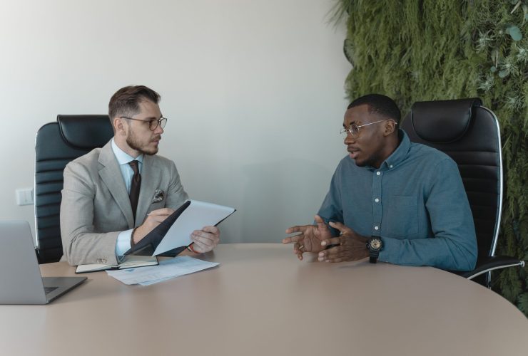 Two men engaged in a behavioral interview, seated at a table, discussing professional experiences and skills.