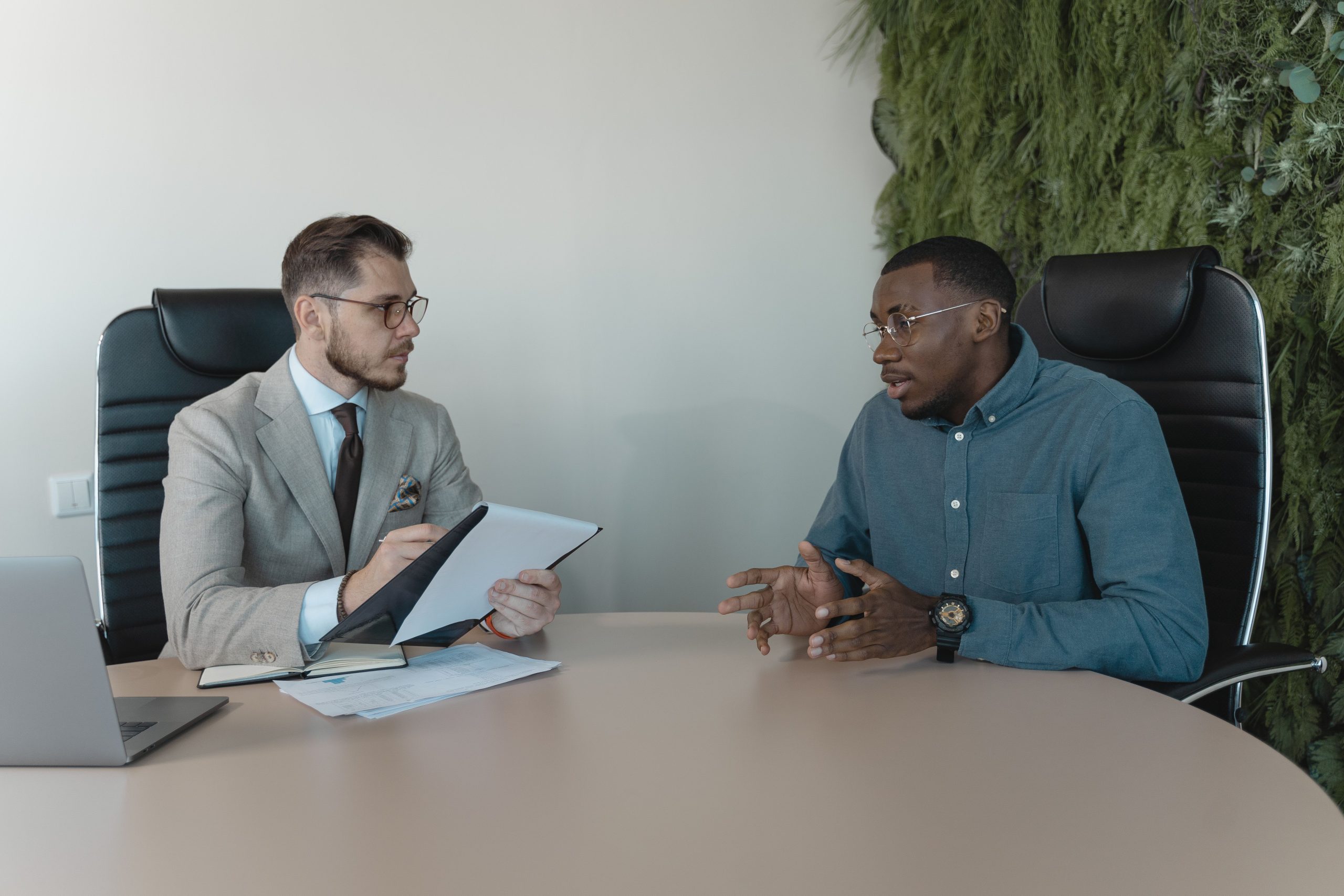 Two men engaged in a behavioral interview, seated at a table, discussing professional experiences and skills.